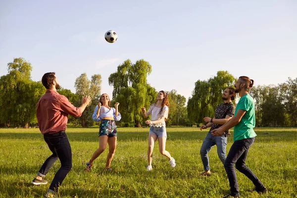 Des amis joyeux jouent avec une balle sur l'herbe dans un parc d'été. — Photo
