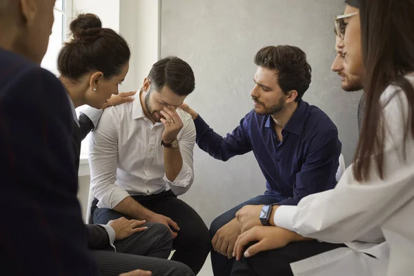 People in a group therapy meeting comforting and supporting a depressed young man — стоковое фото