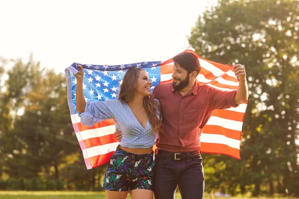 Boldog pár amerikai zászlóval a szabadban. Fiatal férfi és barátnője nemzeti zászlóval ünneplik a függetlenség napját — Stock Fotó