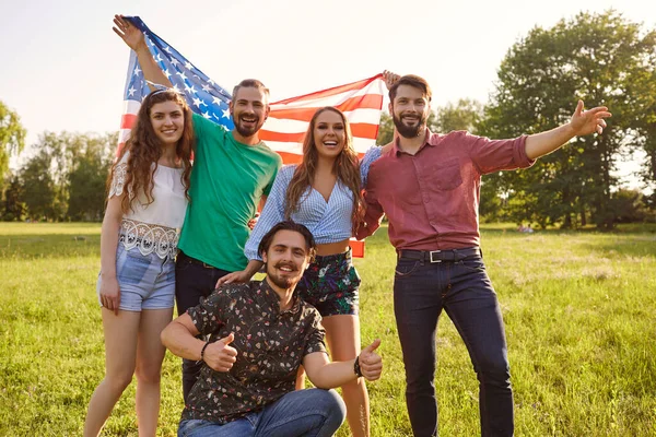 Amerikai zászlóval rendelkező fiatalok csoportja ünnepli Amerika függetlenségének napját a parkban állva. — Stock Fotó