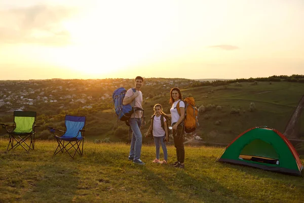 Šťastná rodina na letním tábořišti v horách. Rozkošná dívka a rodiče stojící v kempu během západu slunce — Stock fotografie