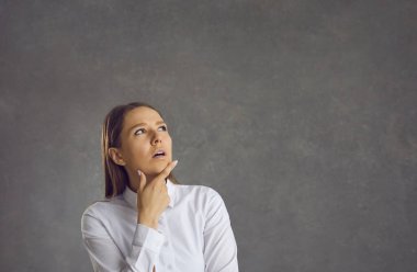 Gri bir arka planda durup çözüm düşünen düşünceli bir kadın..