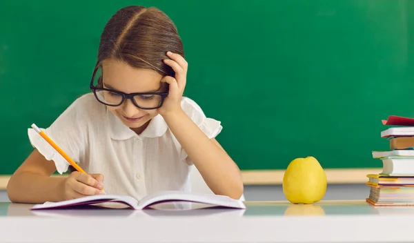 Geconcentreerd schoolmeisje kind schrijven in copy-book terwijl zitten aan de balie — Stockfoto