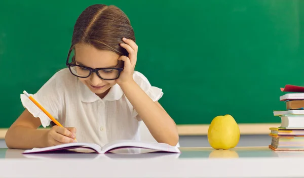 Niño escolar concentrado escribiendo en un libro de texto mientras está sentado en el escritorio — Foto de Stock