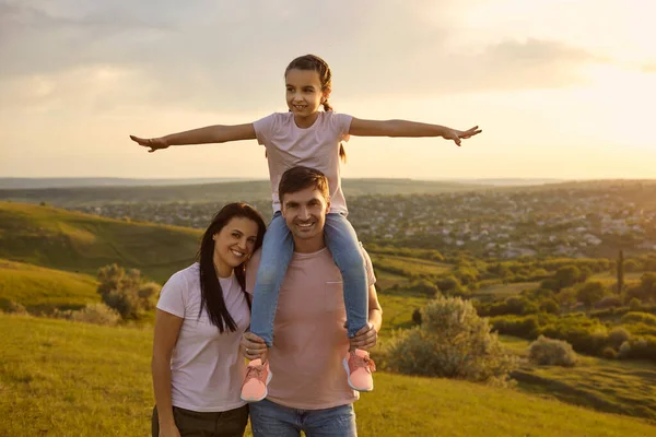 Daughter on the shoulders of parents smiling walk on the grass at sunset in nature. — 스톡 사진