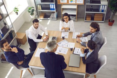 Şirket toplantısında ofis masasında oturan üst düzey yöneticileri dinleyen genç işçiler.