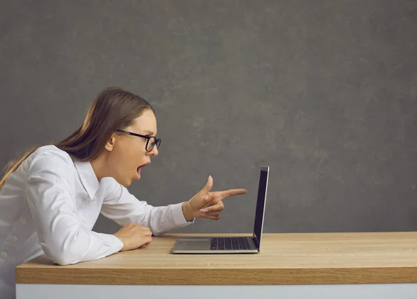 困惑した表情の感情的な女性は、ラップトップの前に座って、画面を指しています. — ストック写真