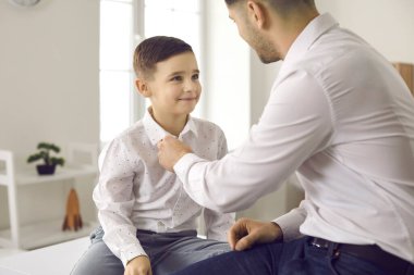 Şık bir aile. Sevgi dolu baba, küçük tatlı oğlunun gömleğine düğme takmasına yardım eder..