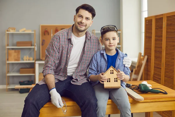 Молодий батько зі своїм коханим маленьким сином сидить на столі в домашній майстерні або гаражі . — стокове фото