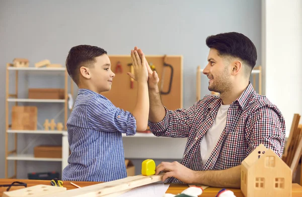 Buon padre sorridente che dà il cinque e sostegno al figlio a casa workshop — Foto Stock