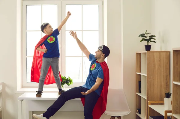 Щаслива впевнена дитина і його тато одягнені як супергерої грають веселі ігри вдома — стокове фото