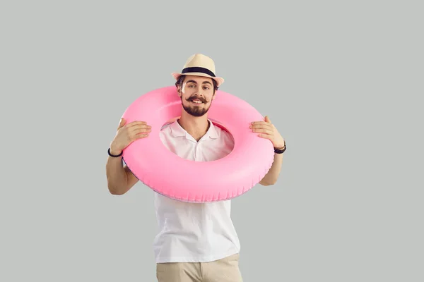 Man met een roze opblaasbare rubberen ring om zijn nek staat op een grijze achtergrond. — Stockfoto