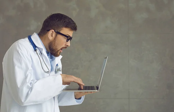 Side view of a shocked male doctor looking at a laptop screen and seeing a medical error. — Fotografia de Stock