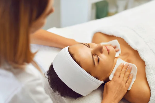 Cosmetologist or masseur wiping relaxing womans neck after facial massage in beauty salon — Zdjęcie stockowe