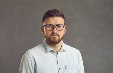 Gri arka planda ciddi yüz ifadesi olan bin yıllık bir adamın stüdyo resmini kapat..