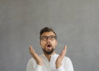 Şaşırmış beyaz adamın yanına yaklaş. İki elini kaldır ve gri arka planda kafasını kaldır..