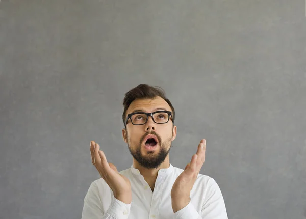 Close up of surprised caucasian man raises two hands and looks up over his head on gray background. — Stockfoto