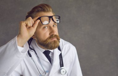 Doktorun yakın plan portresi. Şaşkınlık dolu bir yüz ifadesi. Çıkar gözlükleri.