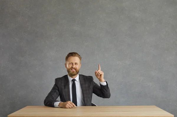 Sorrindo empresário positivo em terno formal tem ideia sentar-se na mesa estúdio tiro — Fotografia de Stock