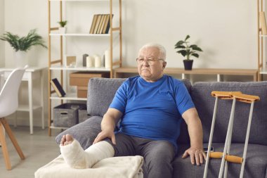 Hayal kırıklığına uğramış olgun bir adam koltukta kırık bacakla oturuyor.