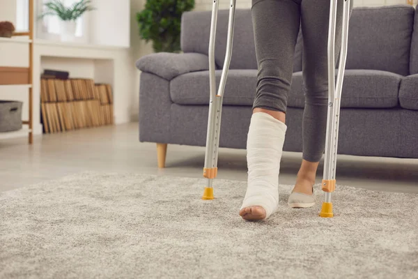 Patient with broken leg in cast stands up from sofa and walks at home using crutches — 스톡 사진