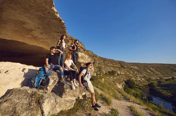 Group of young smiling tourists hikers having rest on natural rocks and enjoying green valley landscape — ストック写真