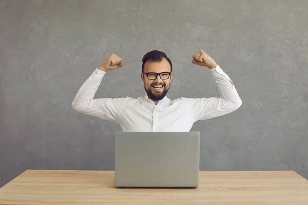 Cheerful strong employee or businessman sits in front of a laptop and shows biceps muscles. — Stock fotografie