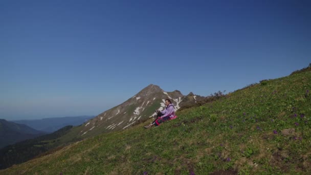 Turista v horách, odpočívá na svahu za slunečného počasí, letecký výhled — Stock video