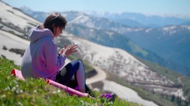 Dağın tepesinde akıllı telefonu olan bir kadın, dağlarda yürüyüş yaptıktan sonra dinleniyor.