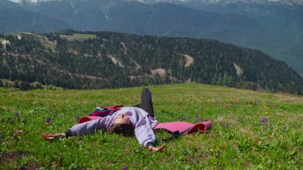Mladá cestovatelka leží na trávě na svahu hory a odpočívá po lezení — Stock video