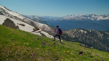 Dağın tepesine tırmanırken, sırt çantalı kadın yamaçta yürüyüş direkleri ile yürüyor.
