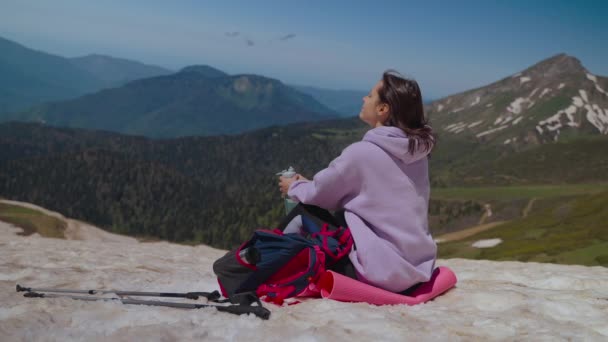 Pihenő turista nő a hegy tetején hegymászás után, nő ül a havon, és csodálja a természetet — Stock videók