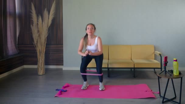 Sportig kvinna knäböjer med elastisk tejp på benen, tränar sin kropp för snygg — Stockvideo