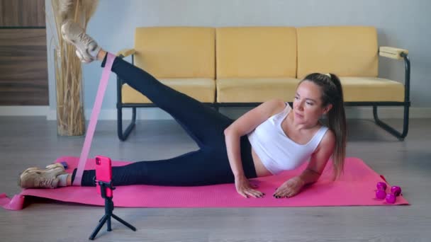 Fata care exercită cu bandă elastică în urma tutorialului de antrenament pe mobil — Videoclip de stoc