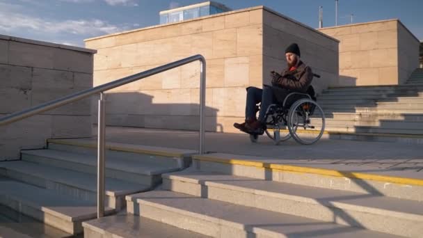 Tekerlekli sandalyedeki engelli adam şehrin ön merdivenlerinde duruyor, akıllı telefon uygulamasındaki haritayı kullanıyor. — Stok video