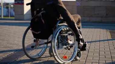 Tekerlekli sandalyedeki adam modern şehirde yolda ilerliyor. Engelliler için ekipman.