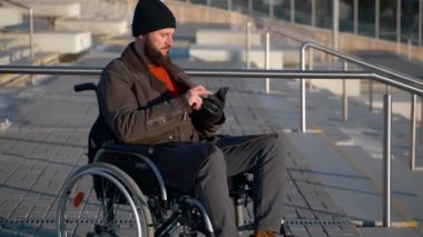 Şehirde yürüyen tekerlekli sandalyeye bağlı bir adam, akıllı telefondan sosyal ağlar kullanıyor.