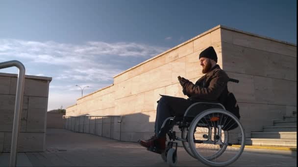 Σωματική αναπηρία και το πρόβλημα με τη μετακίνηση στην πόλη, ο άνθρωπος σε αναπηρική καρέκλα χρησιμοποιεί smartphone — Αρχείο Βίντεο