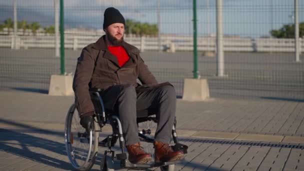 Hombre discapacitado barbudo está conduciendo silla de ruedas manual en la calle de la ciudad, discapacidad e inmovilidad — Vídeo de stock