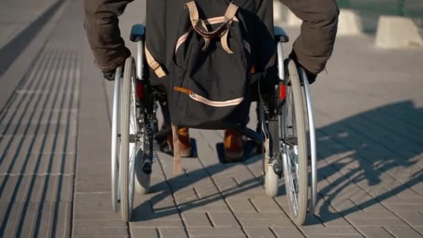 Mężczyzna na wózku inwalidzkim porusza się po ulicy przy słonecznej pogodzie, widok z tyłu — Wideo stockowe