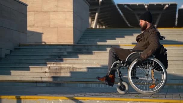Άνθρωπος σε αναπηρική καρέκλα κινείται κοντά σκάλα στο δρόμο της πόλης, μη εξοπλισμένη περιοχή — Αρχείο Βίντεο