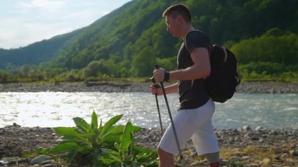Man backpacker med protes ben är promenader över stranden av floden på sommaren — Stockvideo
