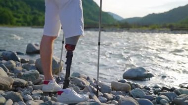 Protez bacaklı mutlu adam dağ nehri kıyısında doğaya hayran.