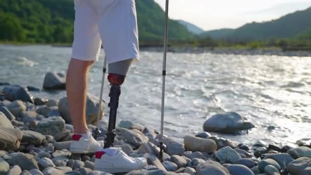 Szczęśliwy człowiek z protezą nogi podziwia przyrodę na wybrzeżu górskiej rzeki — Wideo stockowe