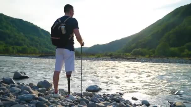 Gehandicapte backpacker bewonderende rivier en berg scene — Stockvideo