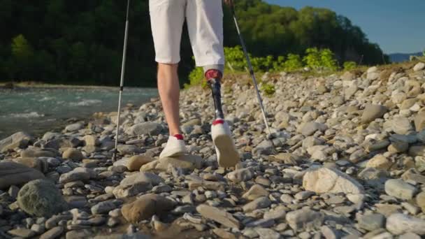 Uomo con gamba protesica è trekking da solo, camminando sulla costa rocciosa del fiume — Video Stock