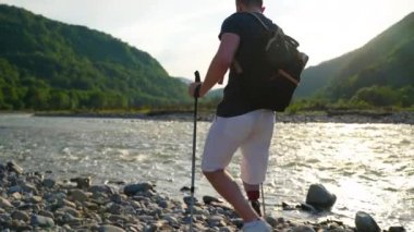 Engelli erkek gezgin doğa yürüyüşü yapıyor, nehir kıyısında yürüyor.