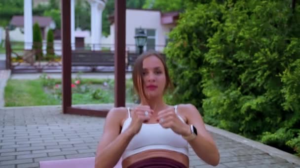 Pretty young woman is training alone in park, doing sit-ups exercise and striking by hands — Wideo stockowe