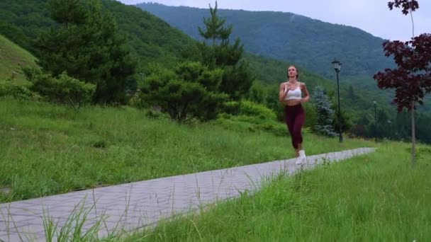 Sportswoman jogging in scenic green park — Video