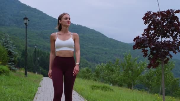 Young sporty woman is walking in park and admiring nature after workout — Vídeo de stock